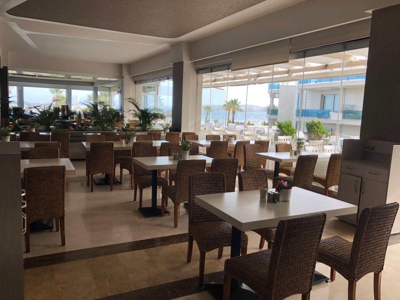 Helles Restaurant mit geflochtenen Stühlen, quadratischen Tischen und großen Fenstern mit Meeresblick.