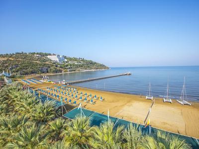 Pláž se žlutým pískem, lehátky a klidným mořem pod jasnou oblohou.