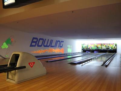 Moderní bowlingová dráha s několika dráhami a dřevěnou podlahou za tlumeného osvětlení.