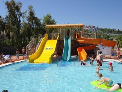 Wasserpark mit Rutschen in Gelb, Blau und Orange, Menschen spielen im blauen Pool unter blauem Himmel.