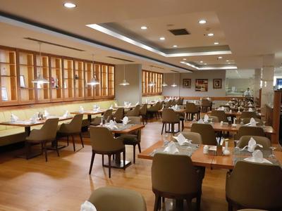 Großer Restaurantraum mit Holzmöbeln, gedeckten Tischen und beige-grünen Stühlen.