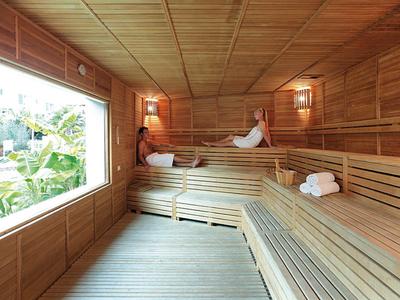 Sauna mit Holzwänden, großen Fenster, mehreren Holzliegen und Handtüchern, zwei Personen entspannt.