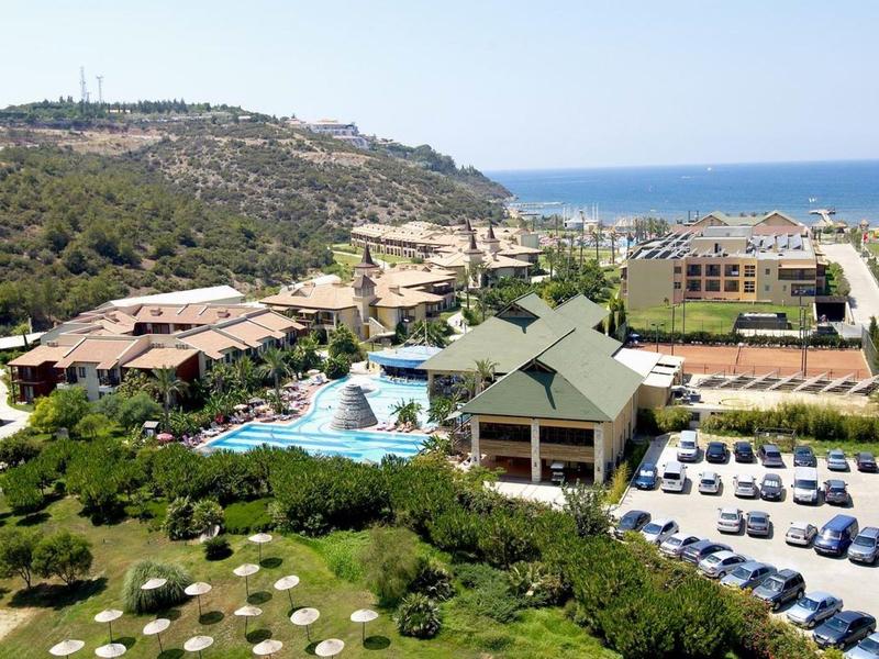 Ferienanlage mit Pool, Grünflächen, Parkplätzen, Hügel und Blick aufs Meer im Hintergrund.