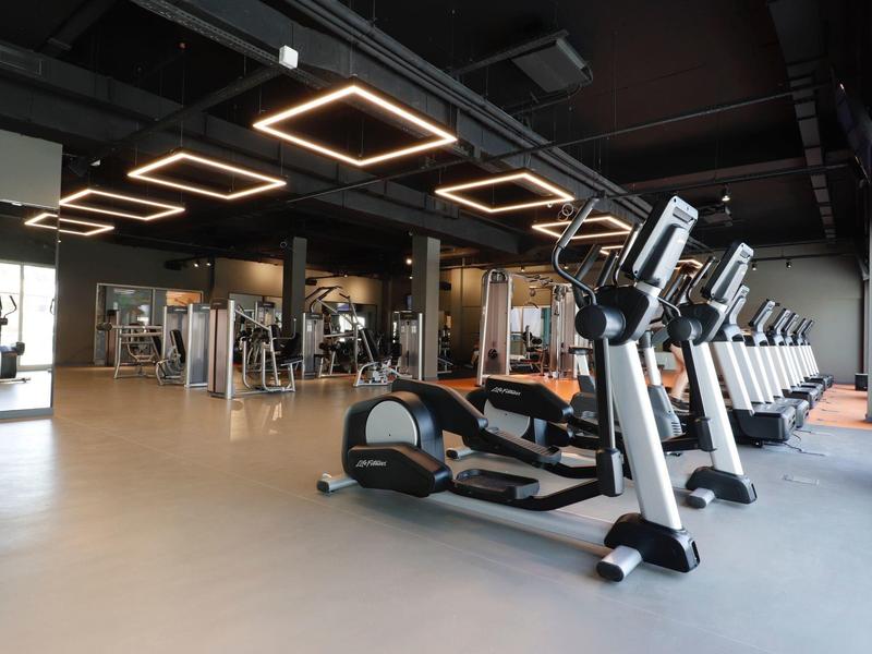 Moderner Fitnessraum mit elliptischen Geräten, Laufbändern und quadratischen Deckenlampen.