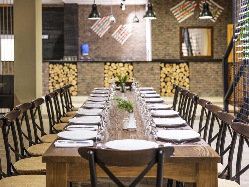 Großer Holztisch im Restaurant, gedeckt mit Tellern und Besteck, von Holzstühlen umgeben.