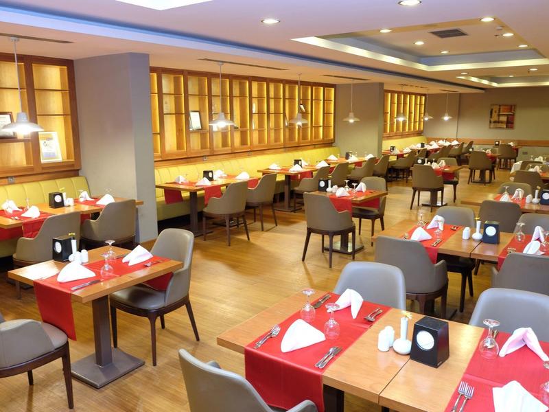 Modernes Restaurant mit roten Tischdecken, grauen Stühlen und hellen Holzmöbeln, gut beleuchtet.