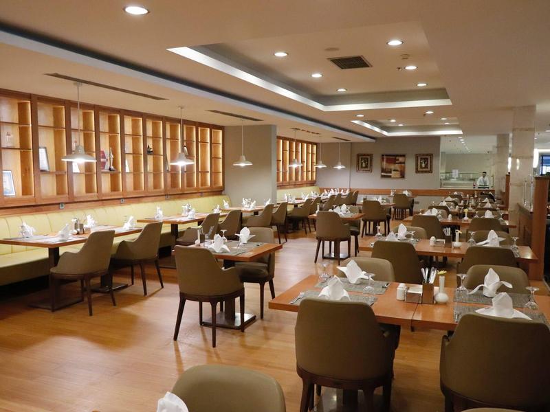 Großer Restaurantraum mit Holzmöbeln, gedeckten Tischen und beige-grünen Stühlen.