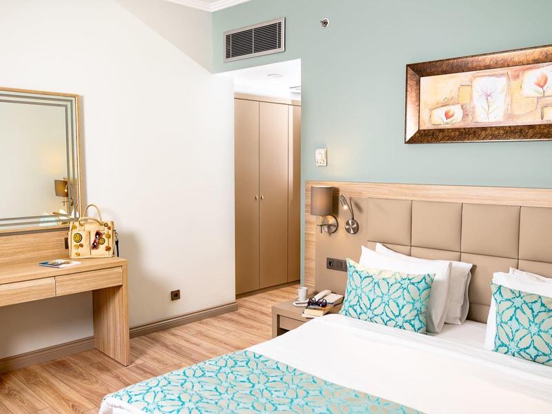 Modernes Schlafzimmer mit Doppelbett, türkis gemusterten Kissen und Holzmöbeln, helle Wände.