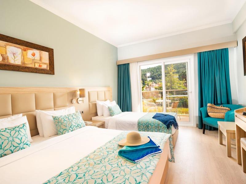 Helles Hotelzimmer mit zwei Betten, türkisfarbenen Akzenten, Schreibtisch und Balkonblick.