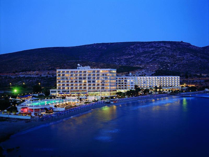 Großes Hotelgebäude mit beleuchteten Fenstern nahe einer ruhigen Küste bei Nacht unter klarem Himmel.