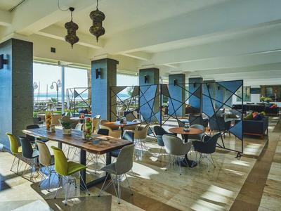 Moderner Speisesaal mit Holztischen, bunten Stühlen, großen Fenstern und eleganter Beleuchtung.