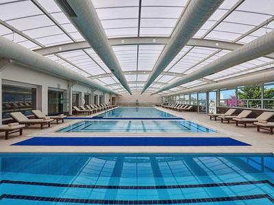 Großes Schwimmbad mit Liegestühlen, Glasdach und separatem Kinderbecken im hellen Raum.