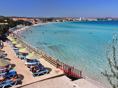 Strand mit Liegestühlen und Sonnenschirmen neben klarem blauem Wasser und blauem Himmel.