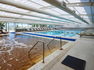 Innen-Schwimmbad mit zwei Becken, Liegestühlen und bodentiefen Fenstern für natürlichen Lichteinfall.