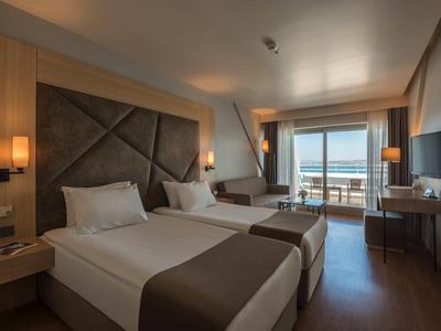 Modernes Hotelzimmer mit zwei Betten, Sitzbereich, TV und großem Fenster mit Meerblick.