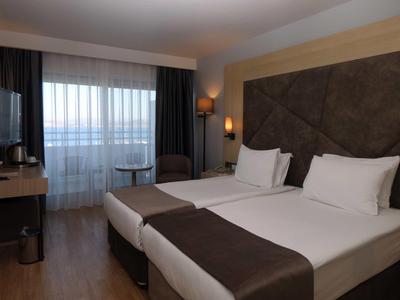 Hell eingerichtetes Hotelzimmer mit zwei Einzelbetten, großem Fenster und Holzboden.