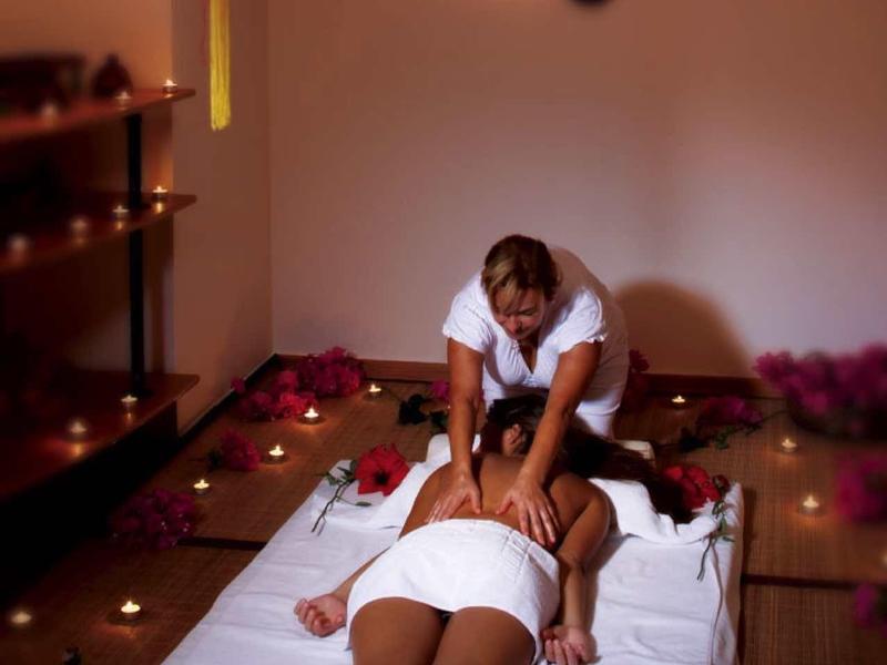 Eine Frau bekommt eine Rückenmassage in einem gedimmten Raum mit Kerzen und asiatischer Dekoration.