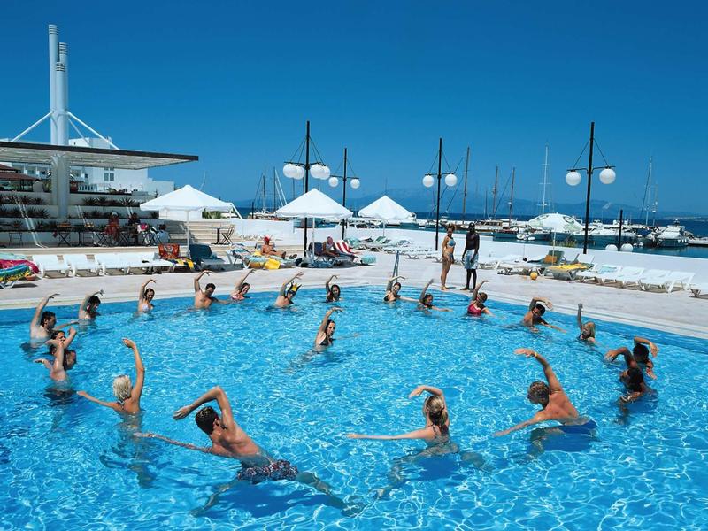 Menschen machen Wassergymnastik im klaren blauen Pool bei sonnigem Himmel am Meer.