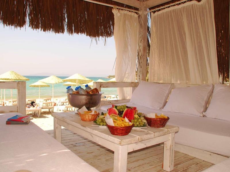 Gemütliche Strandlounge mit weißem Sofa, Holztisch, Früchten und Blick aufs Meer bei Sonnenuntergang.