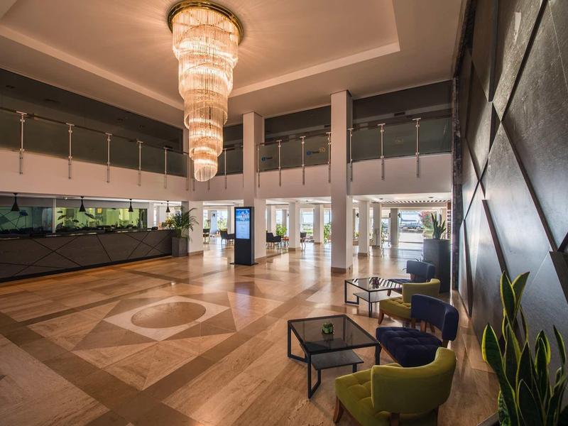 Großer Empfangsbereich mit glänzendem Marmorboden, modernen Sesseln, Pflanzen und Kronleuchter.