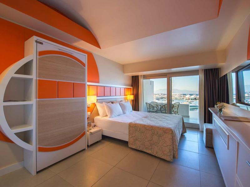 Modernes Hotelzimmer mit Doppelbett, orange-weißer Akzentwand und großem Fenster mit Meerblick.