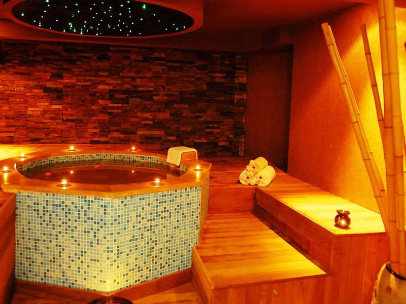 Gemütlicher Wellnessraum mit rundem Mosaik-Whirlpool, Holzbänken und warmem Licht.