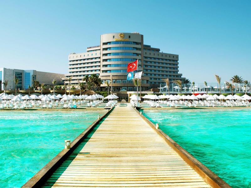 Brettsteg führt zu großem Hotel am türkisfarbenen Meer unter blauem Himmel.
