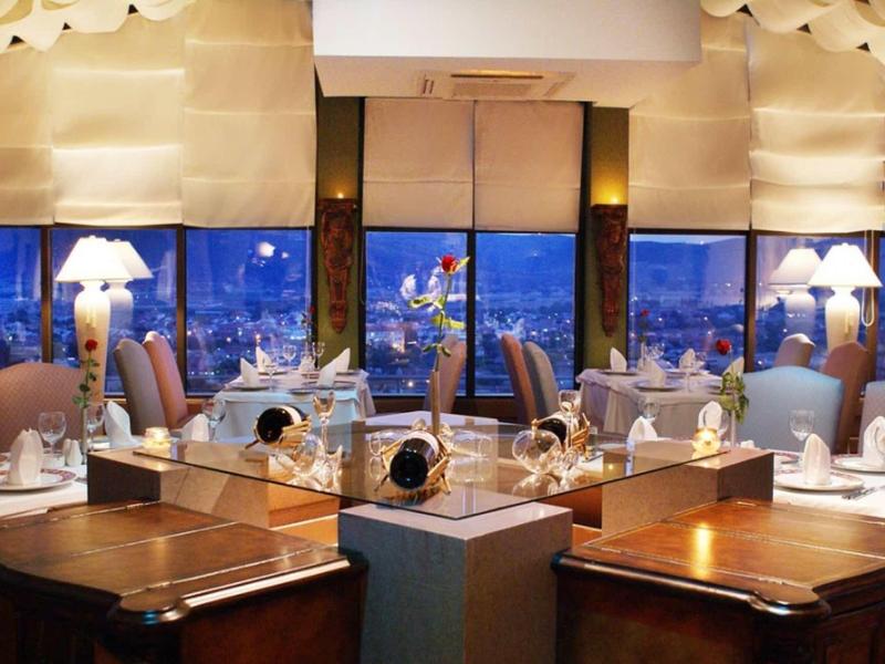 Gemütliches Restaurant mit dunklen Holztischen, weißen Stoffservietten und großen Fenstern bei Abenddämmerung.