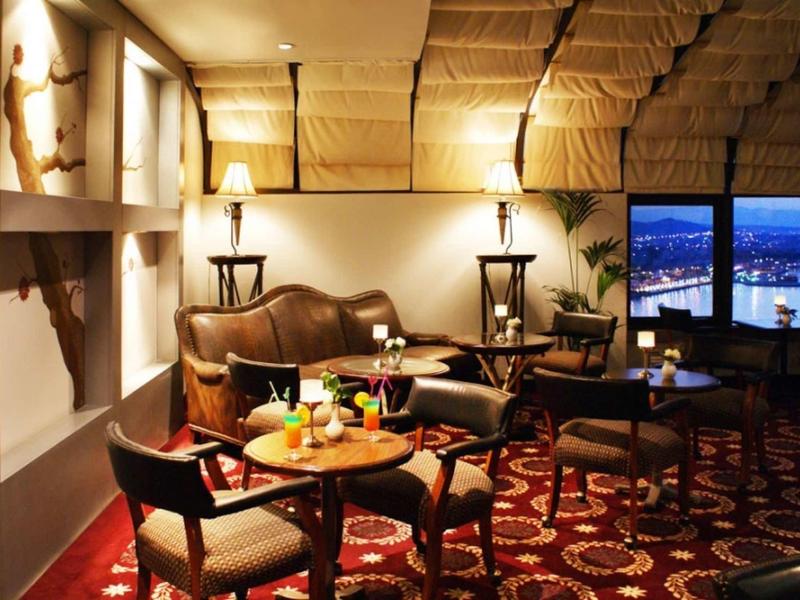 Gemütliche Lounge mit Ledersesseln, Holztischen, Laternen und Teppichboden in warmem Licht.