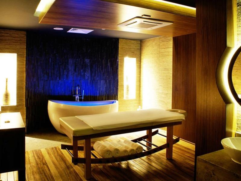 Gemütlicher Wellness-Raum mit Massagebank, warmem Licht und Holzmöbeln, dunklem Vorhang.