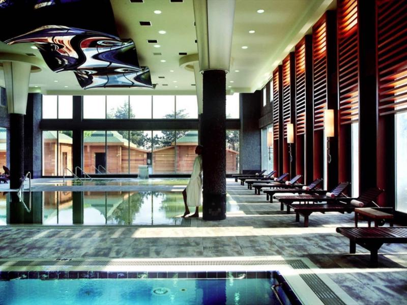 Moderner Innenpool mit hohen Fenstern, Liegen, Holzverkleidung und Deckenbeleuchtung.