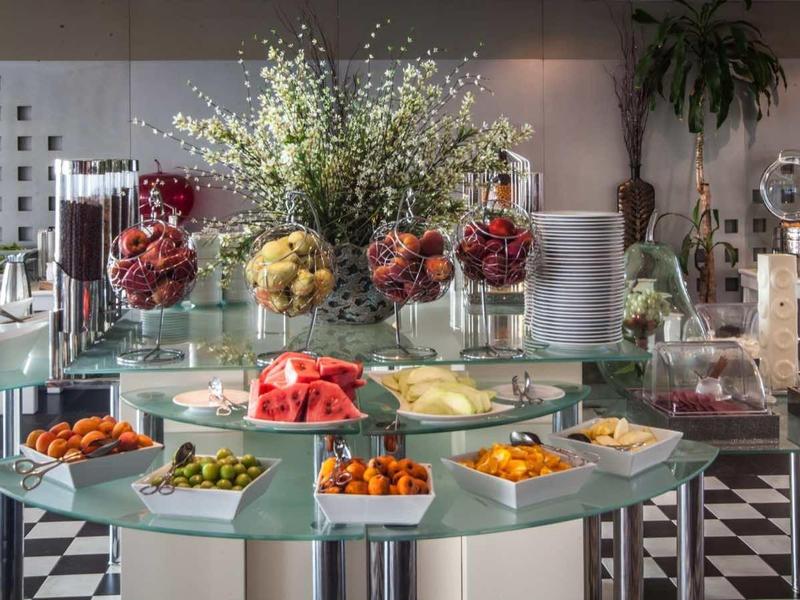 Buffet mit runden grünen Tischen, Obst, Snacks, Blumenarrangement und elegantem Ambiente.