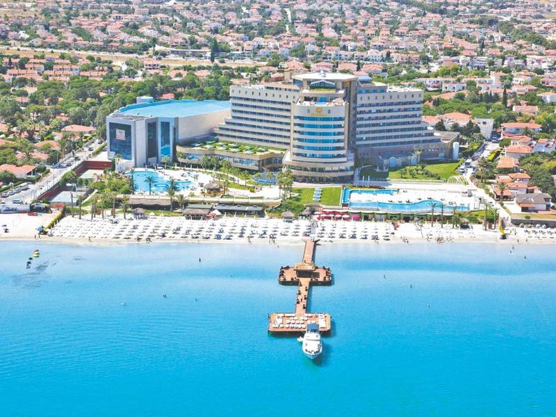 Hotelanlage mit großem Pool, Landungssteg und weißem Sandstrand am türkisblauen Meer.