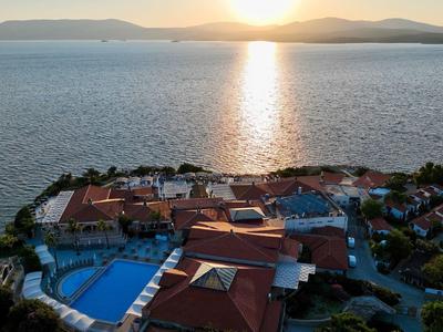 Küstenanlage mit Pool, roten Dächern und Sonnenuntergang über dem ruhigen Meer.