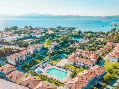Luftaufnahme eines sonnigen Resorts mit großen Pool, roten Dächern und Blick aufs blaue Meer.