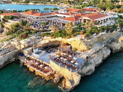 Küstenhotel auf Felsen mit Terrasse, Restauration und klarem türkisfarbenem Meer rundherum.