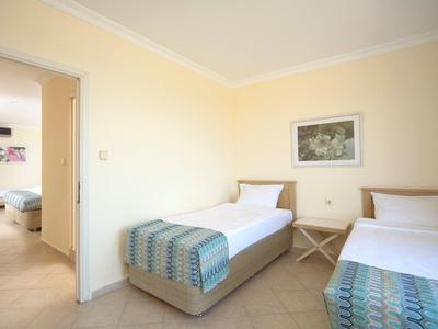 Zwei Einzelbetten mit blauen Tagesdecken in schlichtem, hell gestrichenem Schlafzimmer mit Tür zum anderen Raum.