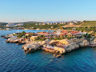 Klippenküste mit Gebäuden, türkisfarbenem Wasser und weiter Landschaft unter klarem Himmel.