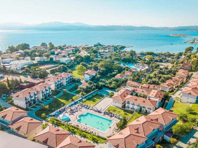 Luftaufnahme eines sonnigen Resorts mit großen Pool, roten Dächern und Blick aufs blaue Meer.