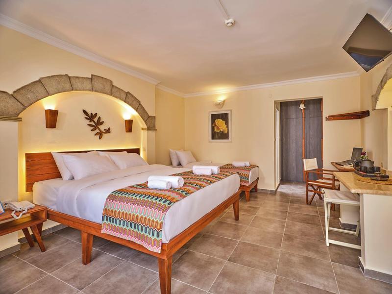 Hell eingerichtetes Schlafzimmer mit Holzbetten, buntem Überwurf und Fliesenboden.