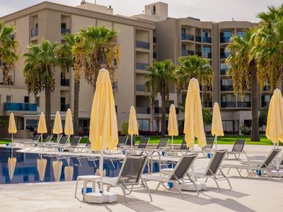 Hotelpool mit gelben Sonnenschirmen und Liegestühlen neben einem mehrstöckigen Gebäude.