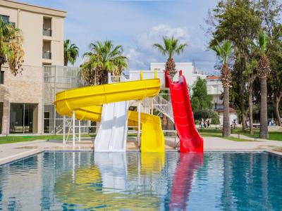 Bunter Wasserrutschenbereich neben einem Pool mit umgebenen Palmen und einem Hotelgebäude im Hintergrund.