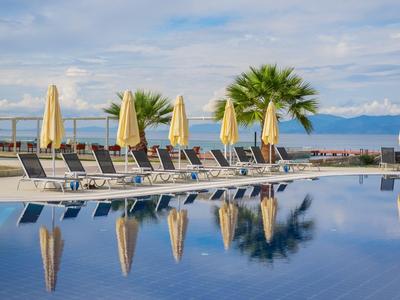 Hotelpool mit Liegestühlen und geschlossenen Sonnenschirmen am klaren Wasser.