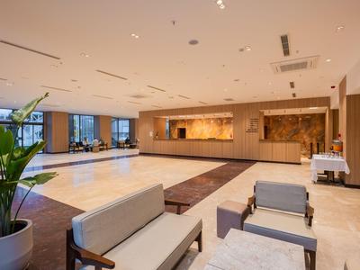 Großer Hotel-Lobbybereich mit hellen Böden, Sitzbereichen und einem Empfangstresen.