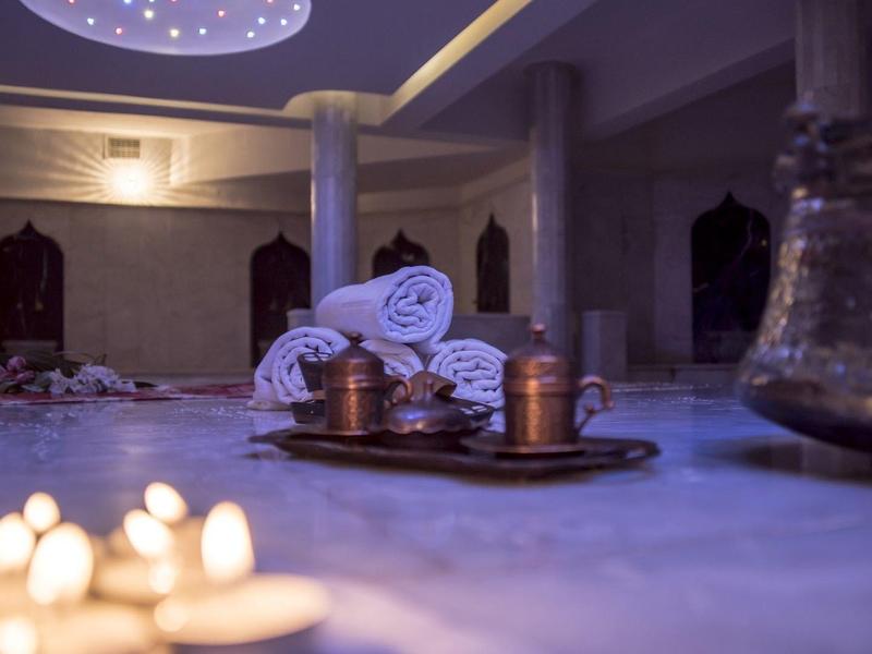 Ein stilvolles, schwach beleuchtetes Spa mit Kerzen, Handtüchern und kupfernen Gefäßen auf einem Tablett.