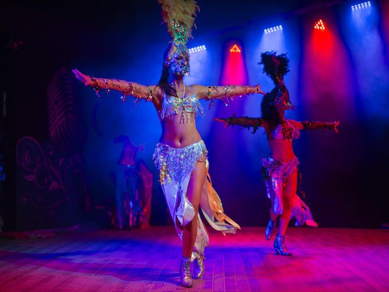 Tänzerin in farbenfrohem Karnevalskostüm mit Federschmuck auf beleuchtetem Bühnenboden.