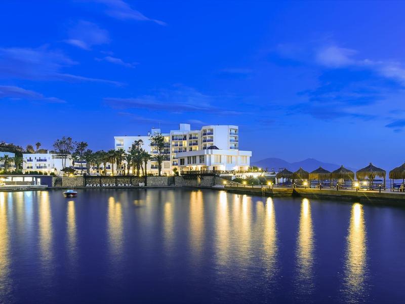 Küstenresort bei Nacht mit beleuchteten Gebäuden und Palmen am ruhigen Wasser.