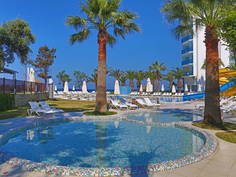 Ein sonniger Poolbereich mit Liegen, Palmen und einem kleinen Rundbecken vor klarem blauem Himmel.