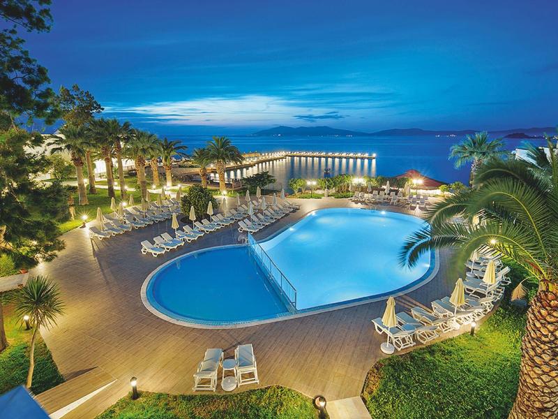 Großer, beleuchteter Pool mit Liegestühlen und Palmen rundherum bei Abenddämmerung am Hotel.