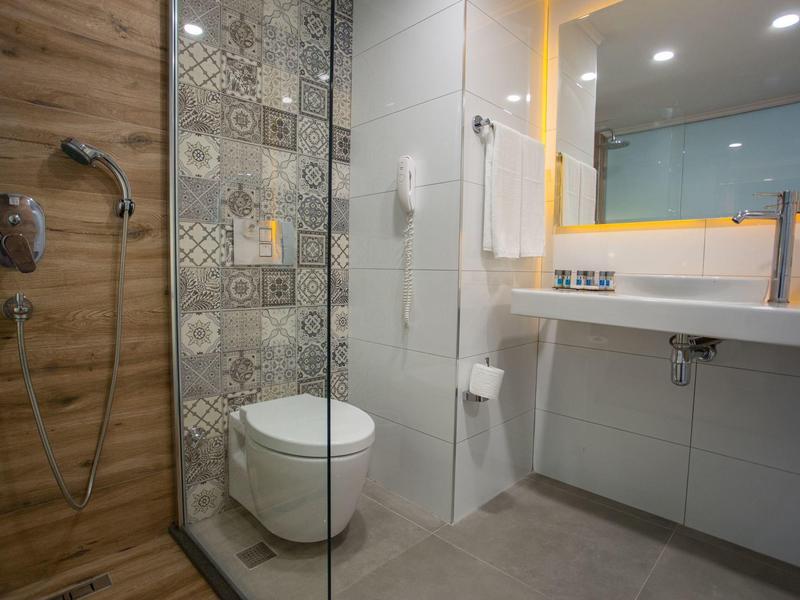 Modernes Badezimmer mit Glasdusche, gemusterter Wandfliese, weißen Sanitäranlagen und großem Spiegel.